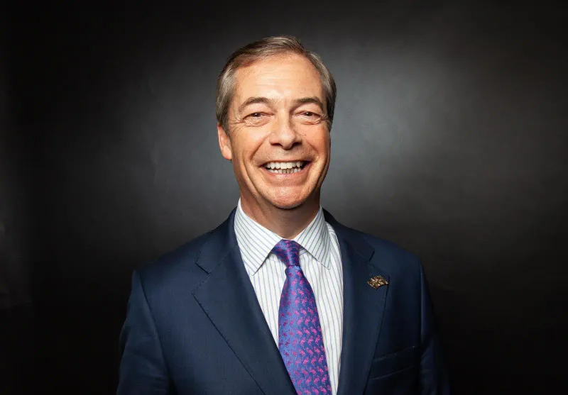 Photo of a smiling man in a blue suit with a colorful tie against a dark background.